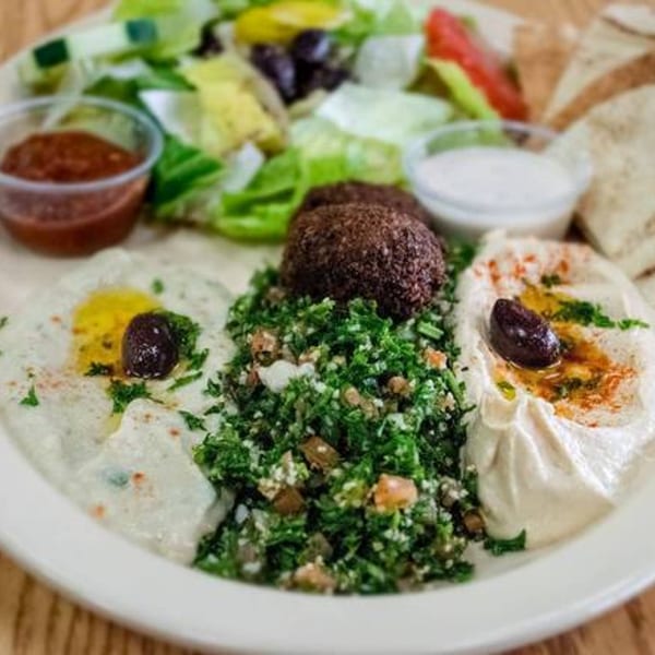 Mediterranean platter with falafel, tabbouleh, hummus, baba ghanoush, salad, pita, and sauces.