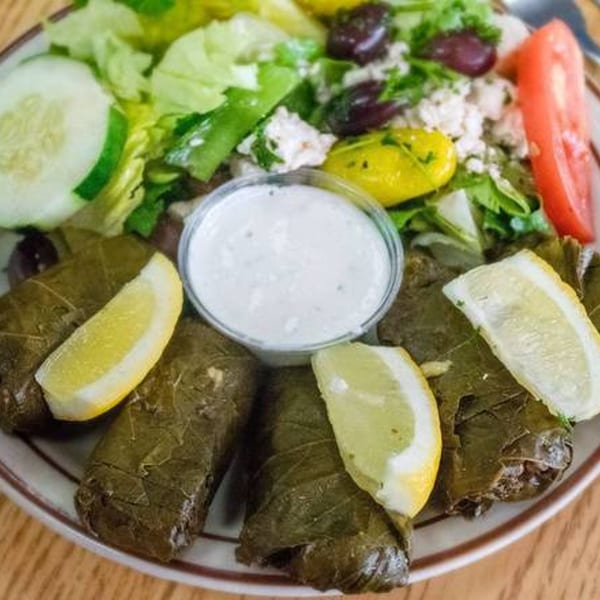 A plate of Mediterranean dolmades with lemon wedges, a side salad, and a cup of tzatziki sauce.
