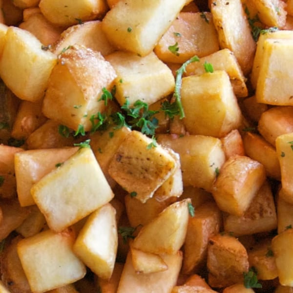 Close-up of golden brown roasted potatoes, seasoned with herbs, filling the frame.