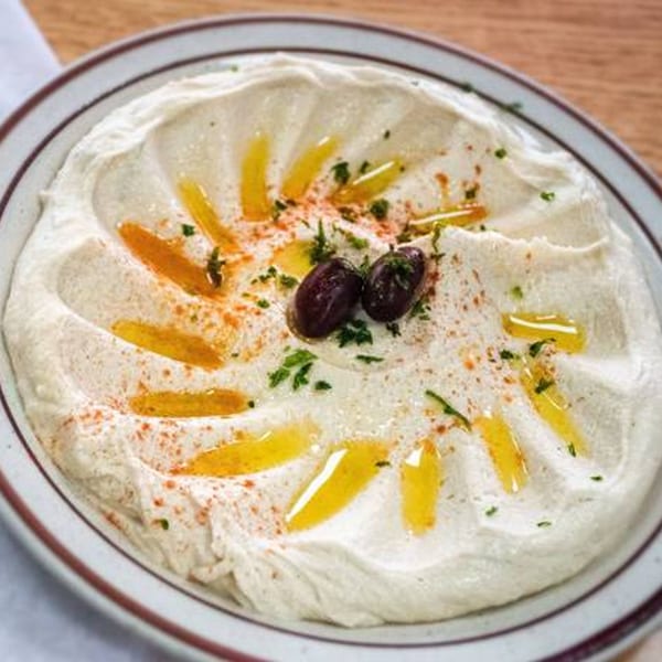 Creamy hummus in a bowl, drizzled with olive oil, paprika, parsley, and two olives.