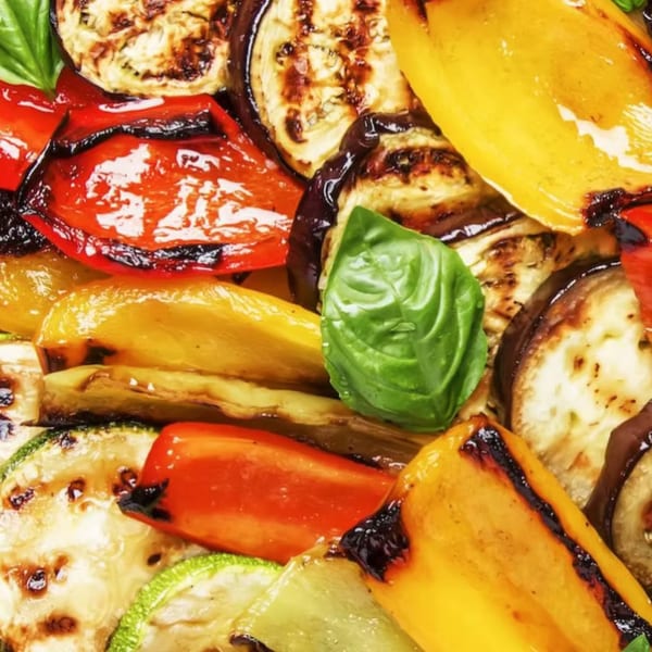 Close-up of grilled red and yellow bell peppers, zucchini, and eggplant slices with a basil leaf.